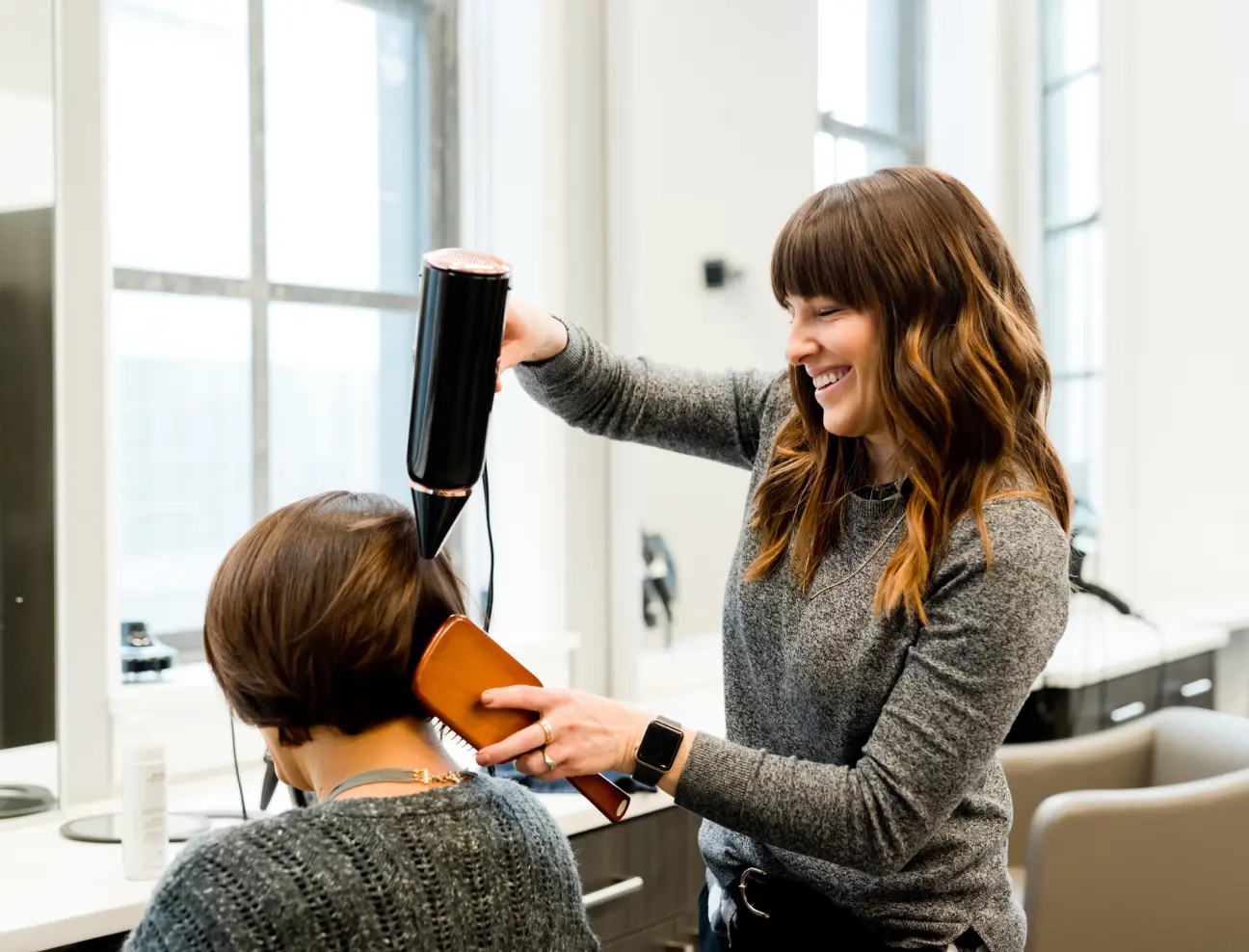 Friseurin beim Föhnen und Stylen der Haare einer Kundin im Salon.