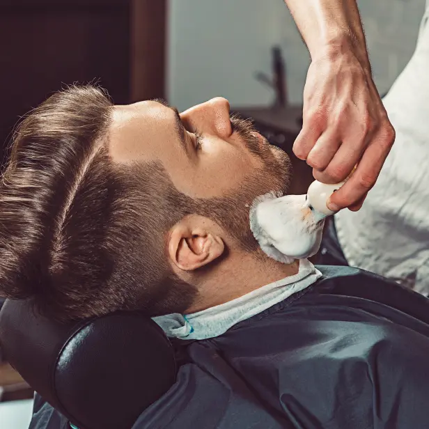Barbier trägt Rasierschaum auf das Gesicht eines Kunden auf.