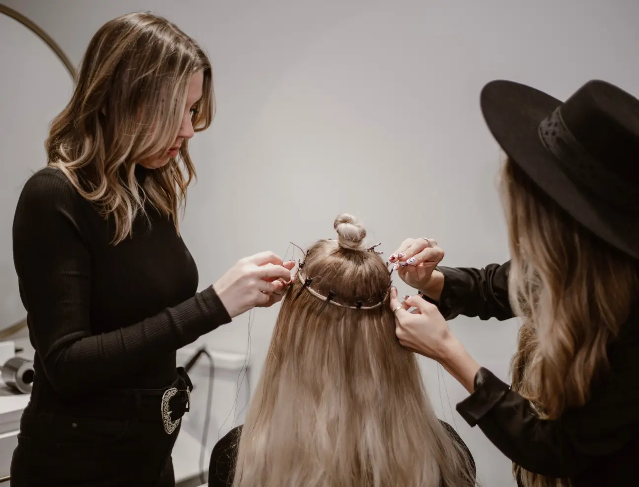 Zwei Friseurinnen arbeiten an einer Haarverlängerung für eine Kundin.